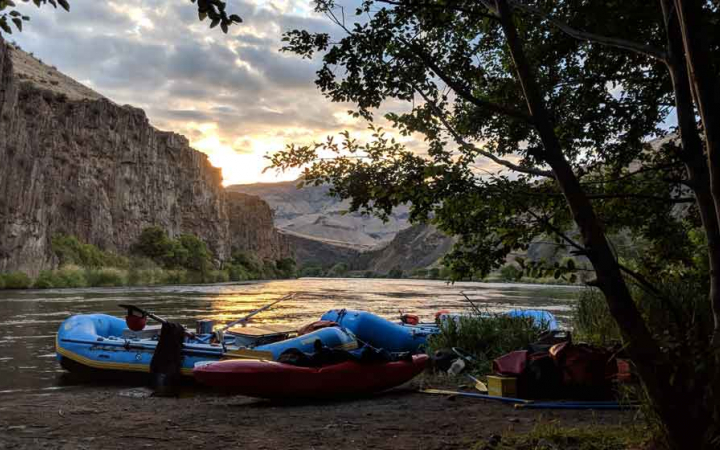 a few rafts rest on the shore of a river at sunset